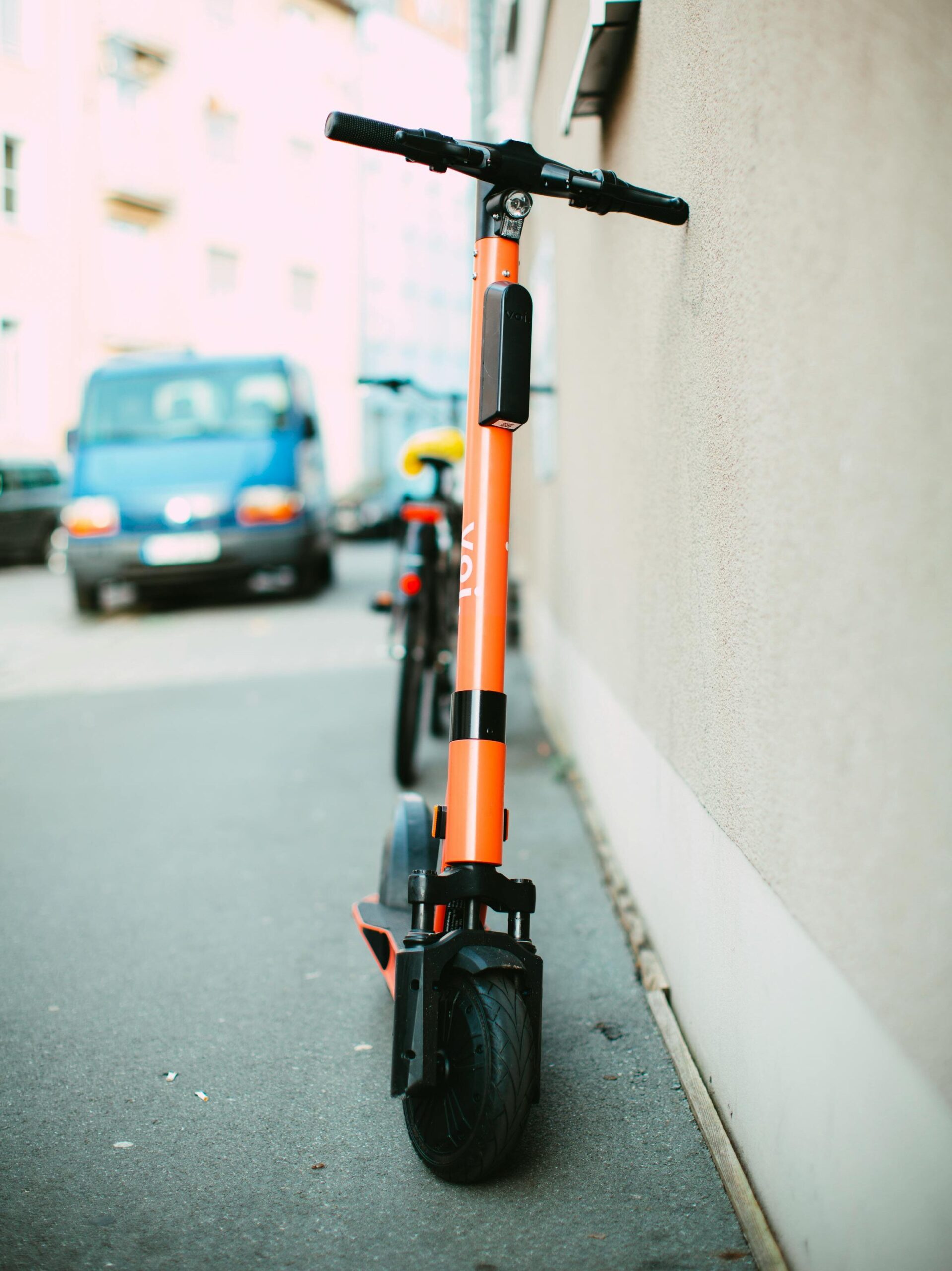 Vibrant orange electric scooter parked on a city sidewalk during daylight, showcasing urban transportation.
