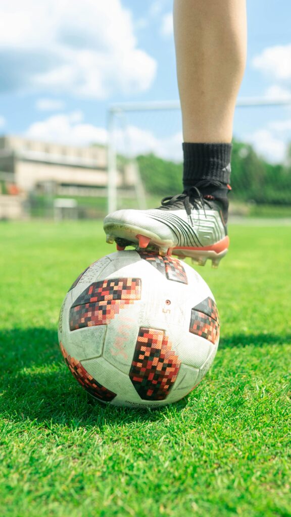 Close-up of a soccer ball with a player's foot on it, set on a vibrant green soccer field during a sunny day.