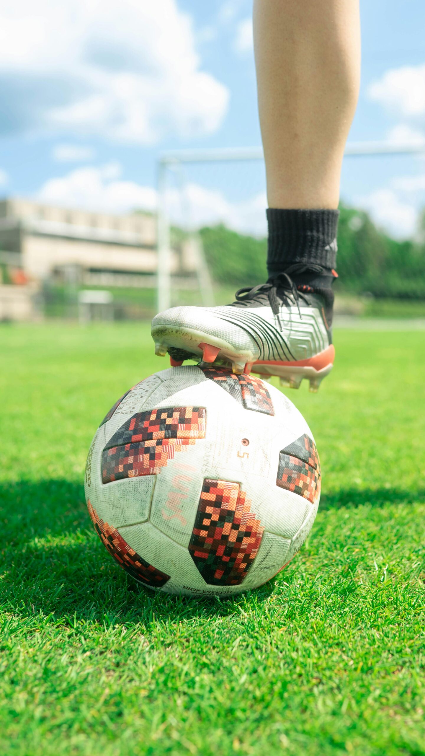 Close-up of a soccer ball with a player's foot on it, set on a vibrant green soccer field during a sunny day.