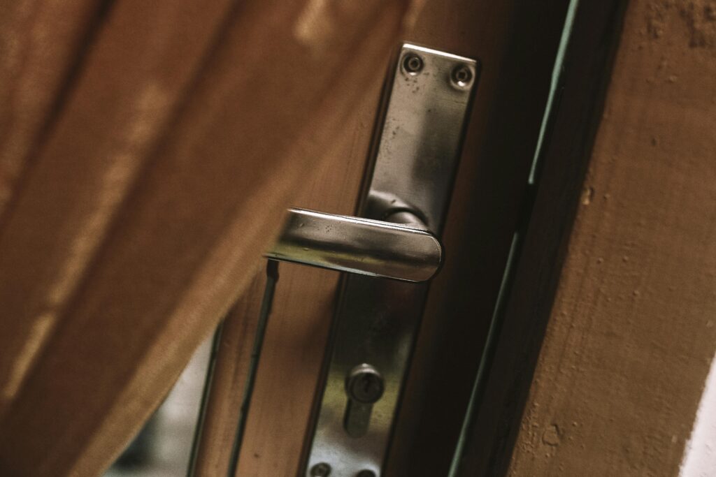 A metal door handle slightly ajar against a wooden background.