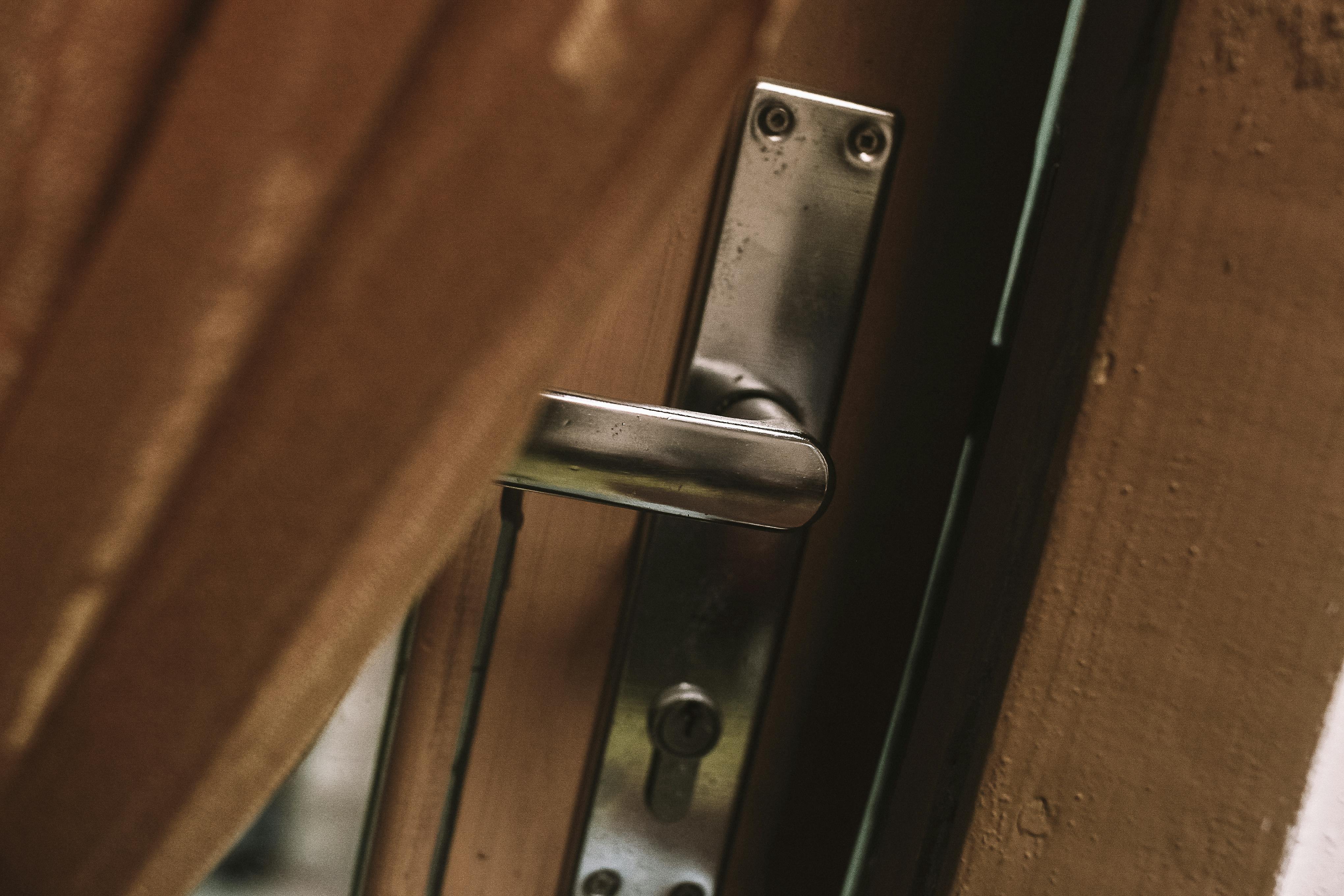 A metal door handle slightly ajar against a wooden background.