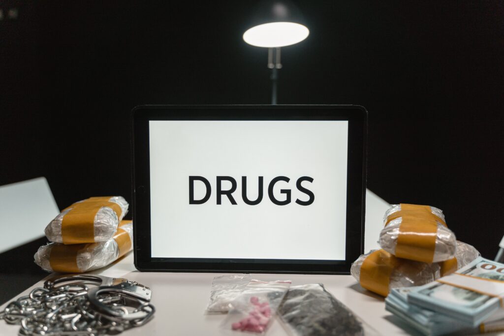 Conceptual image of drugs, money, and handcuffs on a table under harsh light, depicting crime themes.